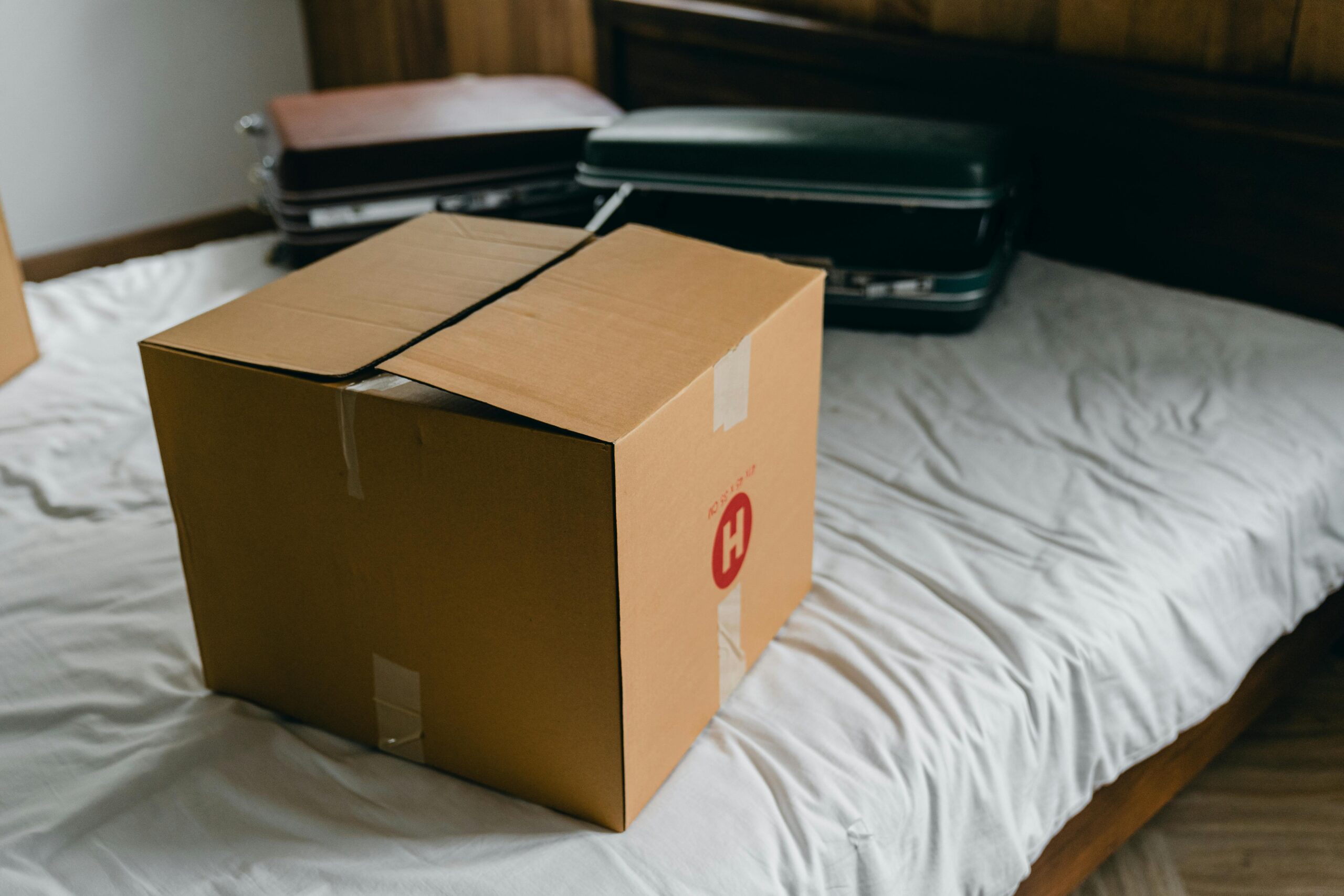 A cardboard box sits on a bed surrounded by suitcases, symbolizing moving or unpacking.